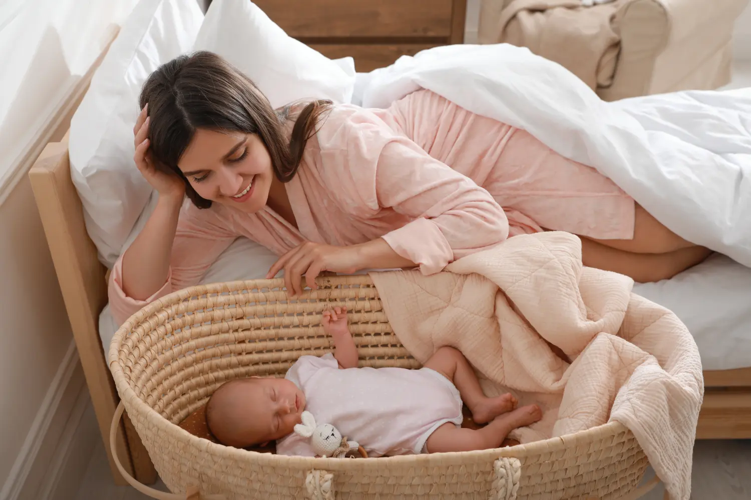 Glückliche junge Mutter ruht in der Nähe der Wiege mit schlafendem Neugeborenen zu Hause