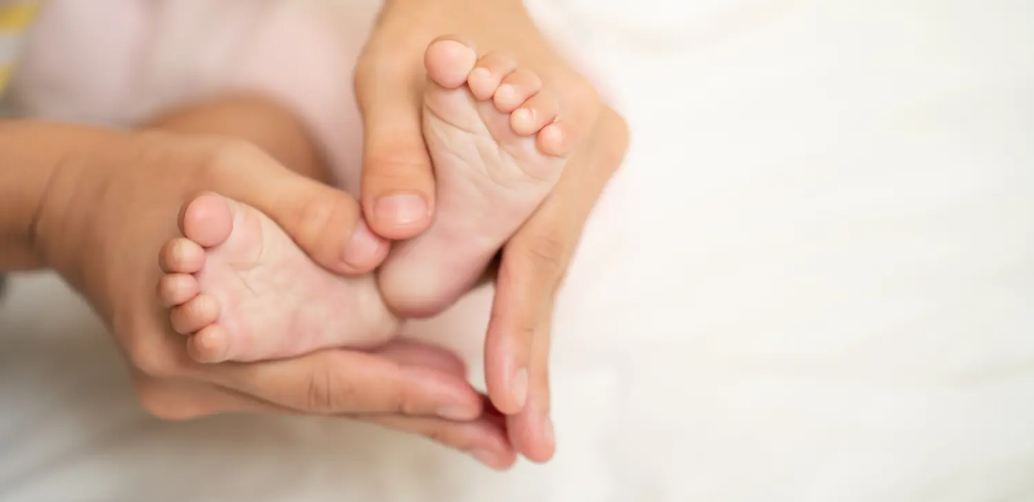 Asiatische Mutterhände in Herzform. Babyfüße in den Händen der Mutter, die ein Symbol der Liebe bedeuten. Mutter und ihr kleines Kind.